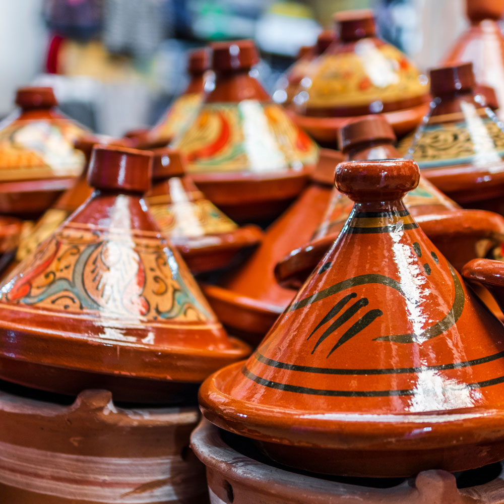 A stack of decorated ceramic tagine pots with conical lids, displayed for sale in a market—perfect inspiration as you plan your luxury culinary or heritage trip to Morocco.