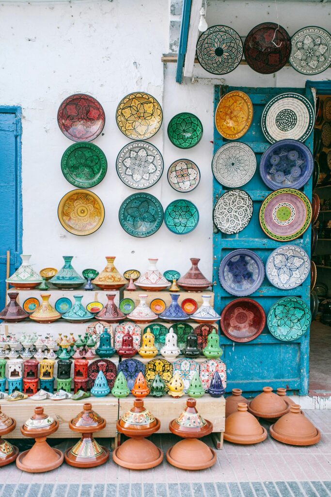 Colorful ceramic plates and tagines are displayed on a white and blue wall outside a shop, arranged neatly on shelves and hanging for sale.